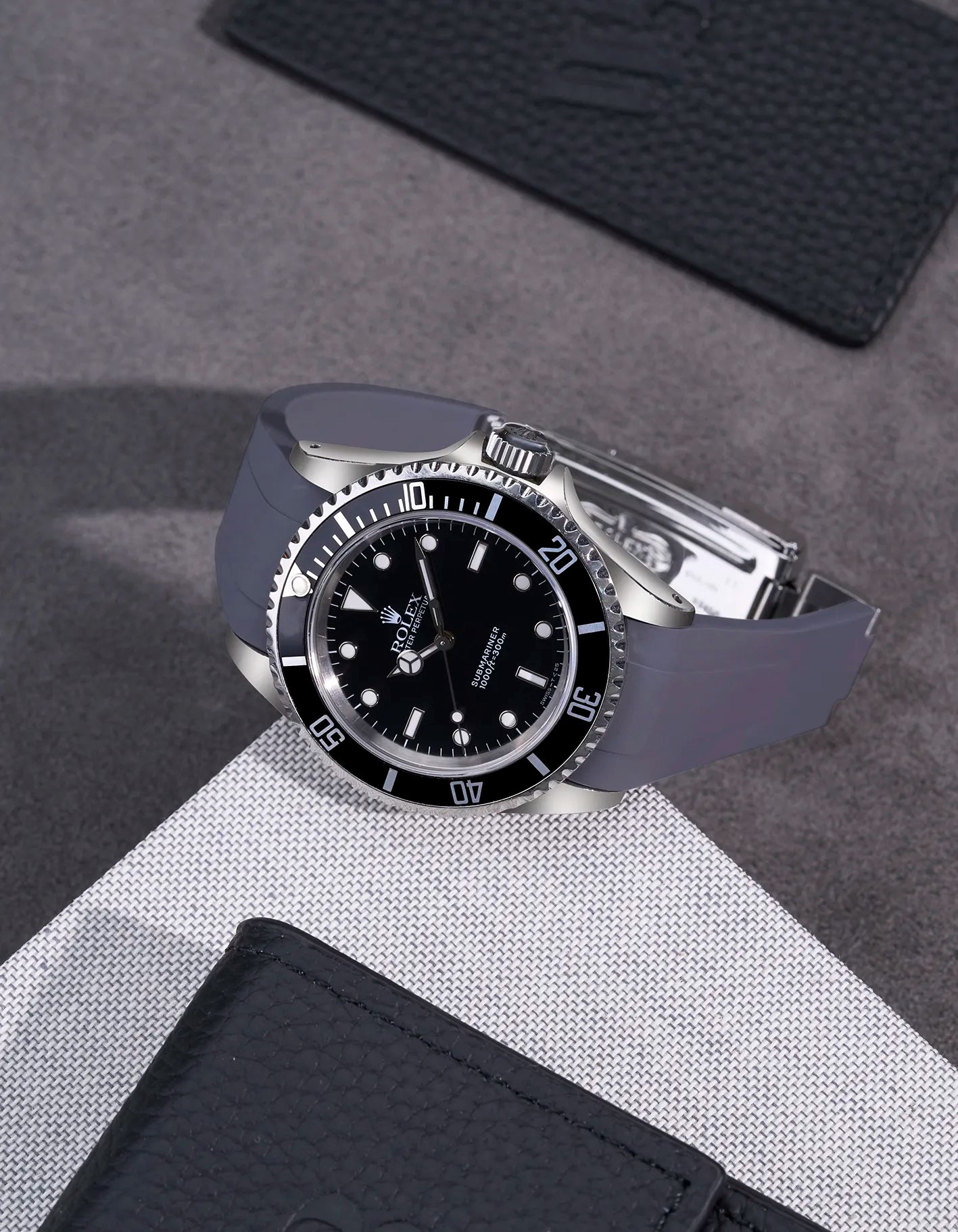 Rolex Submariner 16610 and 14060 with grey integrated FKM rubber strap and original clasp on textured surface