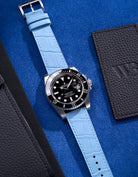 Rolex Submariner watch featuring a light blue alligator leather strap on a bright blue background