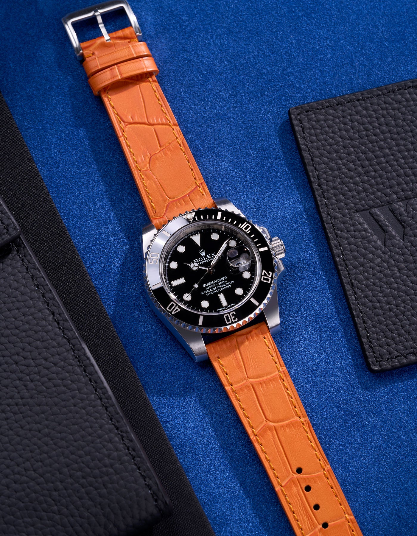 Rolex Submariner with a bold orange alligator leather strap displayed on a vibrant blue surface