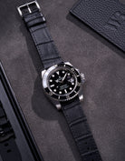 Rolex Submariner with a black alligator leather strap displayed on a dark gray background