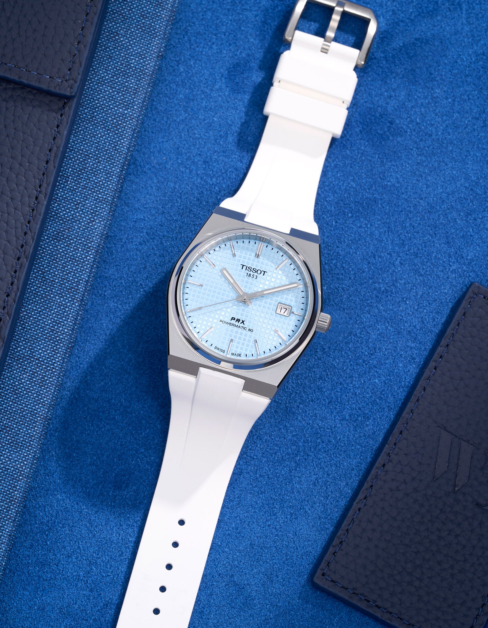 Tissot PRX watch with green dial fitted with white FKM rubber strap lying flat on blue background