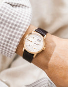 A Lange Shöne in rose gold with a dark brown embossed alligator leather strap from Wristbuddys on a wrist, wearing a green sleeve.