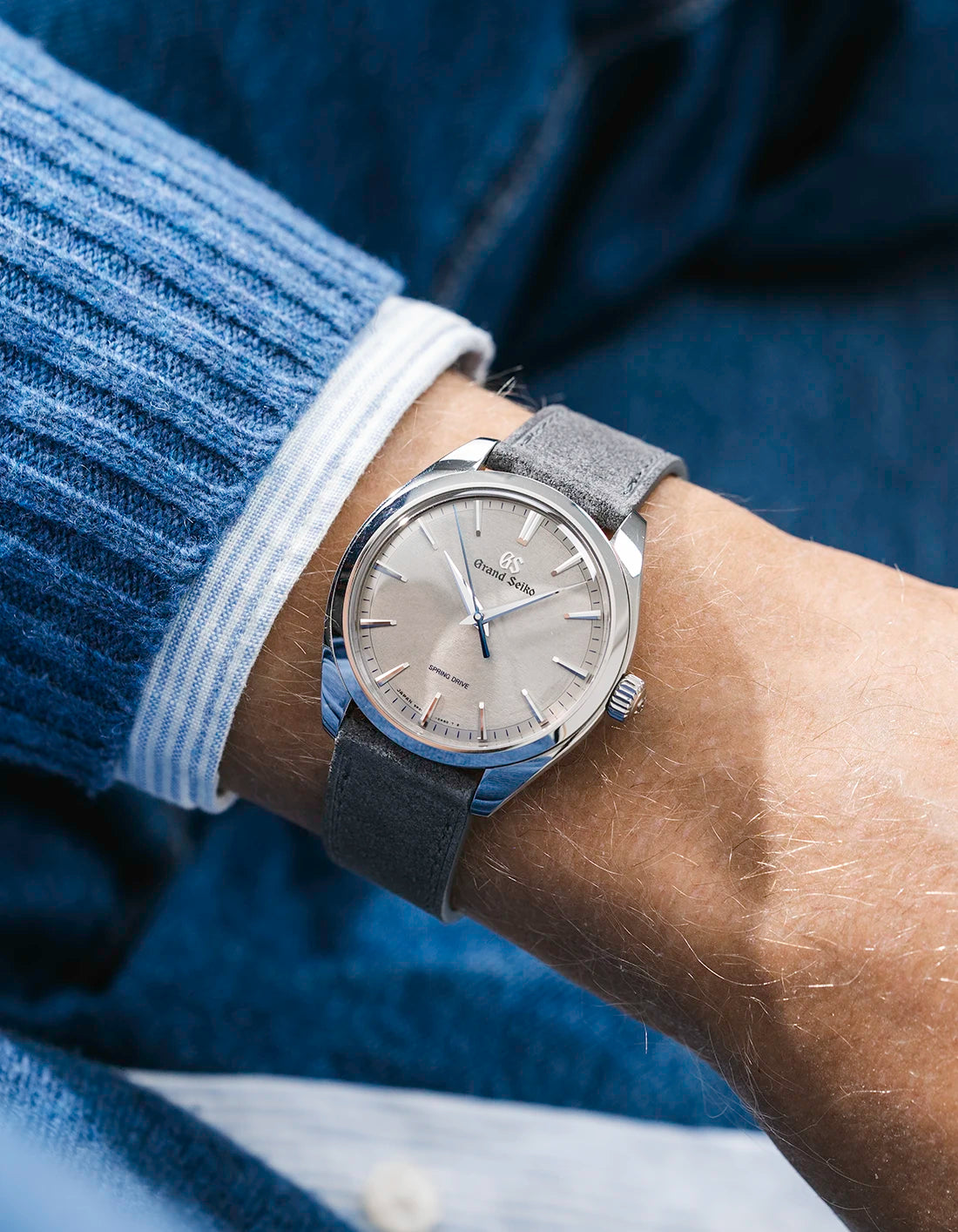 Grand Seiko with a grey suede leather strap from Wristbuddys on a wrist, wearing a blue sleeve.
