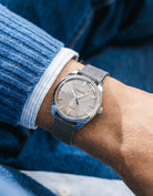Grand Seiko with a grey suede leather strap from Wristbuddys on a wrist, wearing a blue sleeve.