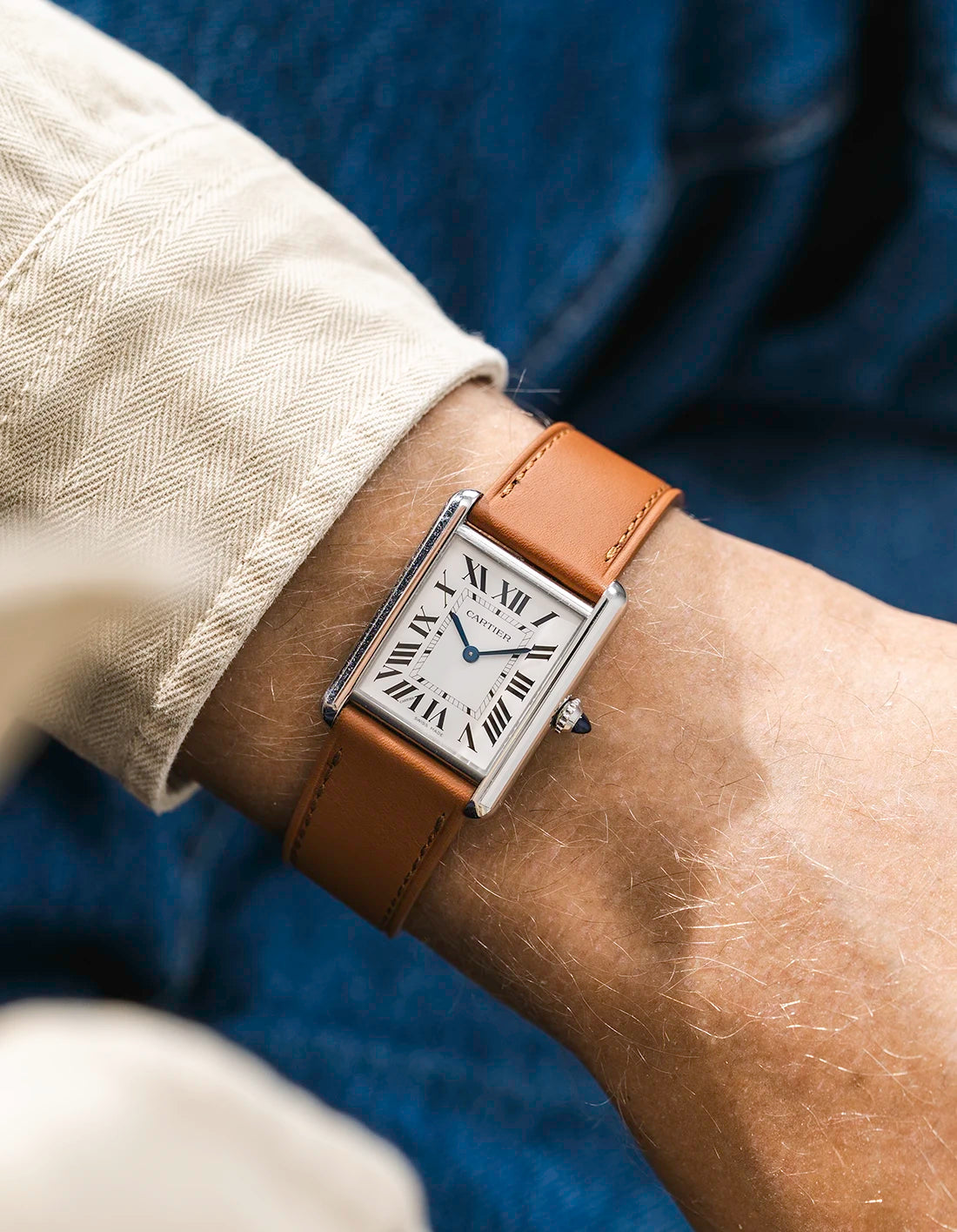 A Cartier Tank Solo with a brown calfskin leather watch strap from Wristbuddys on a wrist, wearing a beige sleeve.