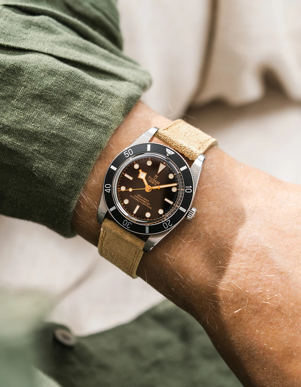 A Tudor BB54 with a beige suede leather strap from Wristbuddys on a wrist, wearing a green sleeve.