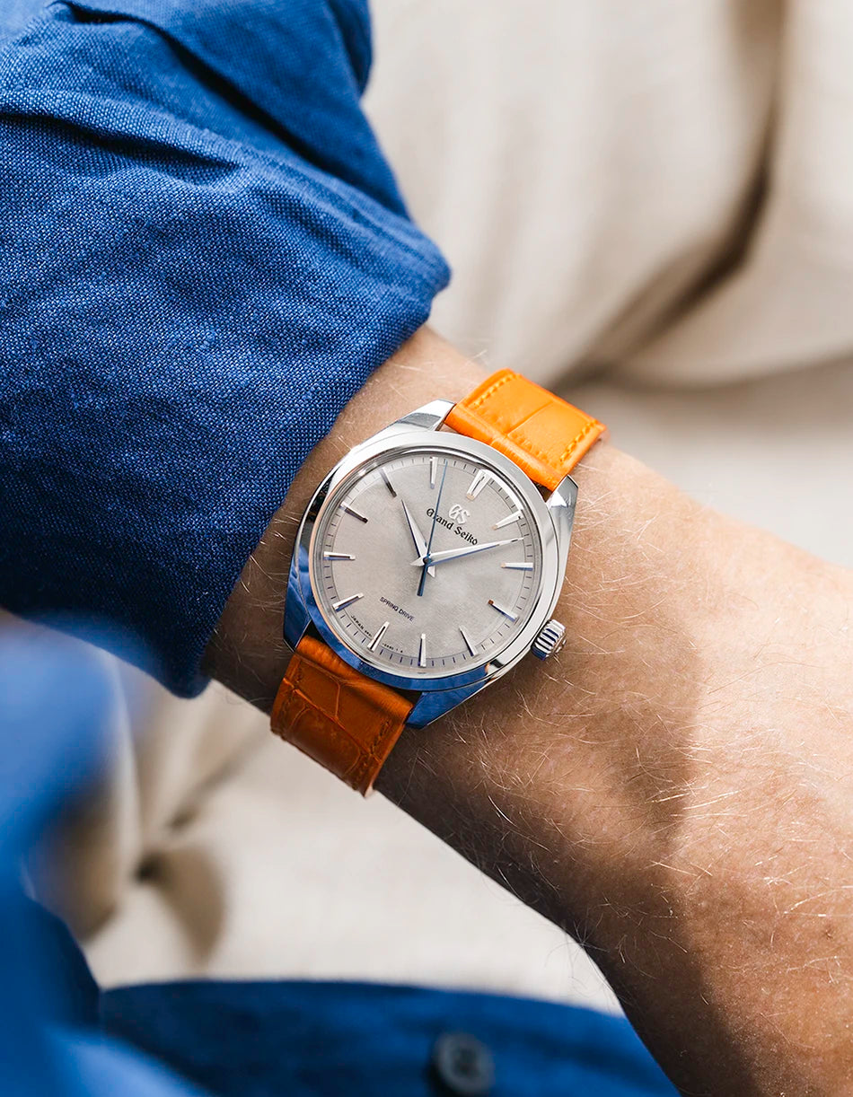Grand Seiko with a orange embossed alligator leather strap from Wristbuddys on a wrist, wearing a blue sleeve.