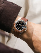 Close-up of a person wearing a Rolex GMT Master 2 Rootbeer with a brown vertech FKM rubber watch strap from Wirstbuddys on a wrist, wearing a striped shirt.