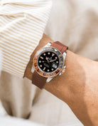 Close-up of a person wearing a Rolex GMT Master 2 Rootbeer with a brown FKM rubber watch strap from Wirstbuddys on a wrist, wearing a striped shirt.

