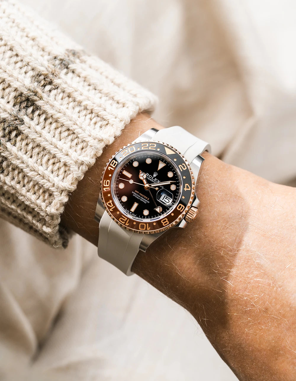 Close-up of a person wearing a Rolex GMT Master 2 Rootbeer with a beige FKM rubber watch strap from Wirstbuddys on a wrist, wearing a striped shirt.