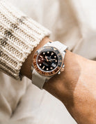 Close-up of a person wearing a Rolex GMT Master 2 Rootbeer with a beige FKM rubber watch strap from Wirstbuddys on a wrist, wearing a striped shirt.