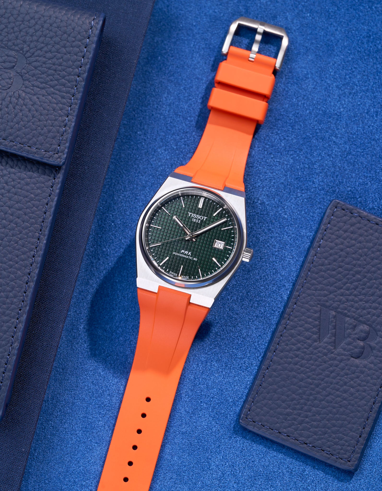 Tissot PRX watch with green dial fitted with orange FKM rubber strap lying flat on blue background