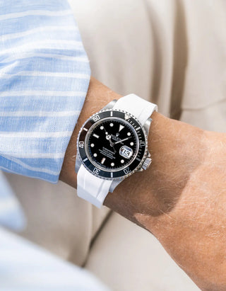 White FKM rubber strap integrated for original clasp on Rolex Submariner 16610LN full steel, black ceramic bezel, black dial, straight front-facing wrist shot, smooth white strap texture, light blue striped linen shirt sleeve, cream background