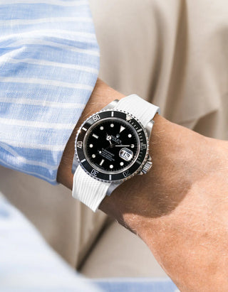 White Vertech FKM rubber strap integrated for original clasp on Rolex Submariner 16610LN full steel, black ceramic bezel, black dial, angled wrist shot from left side, Vertech crosshatch texture clearly visible on white strap, light blue striped linen shirt sleeve, beige background