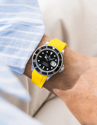 Yellow FKM rubber strap integrated for original clasp on Rolex Submariner 16610LN full steel, black ceramic bezel, black dial, straight front-facing wrist shot, smooth yellow strap, light blue striped shirt cuff, white and beige background