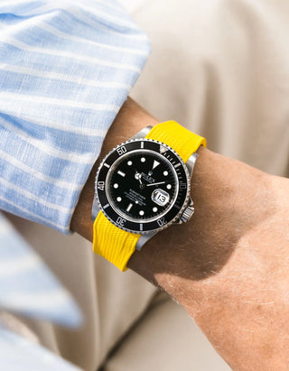 Yellow Vertech FKM rubber strap integrated for original clasp on Rolex Submariner 16610LN full steel, black ceramic bezel, black dial, straight front-facing wrist shot, Vertech crosshatch texture clearly visible on strap, light blue striped shirt cuff, beige background