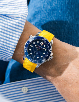 Yellow Vertech rubber strap for Omega Seamaster Diver 300 42mm – worn on wrist with light blue striped shirt, blue dial and bezel, blue jacket background, front angle view