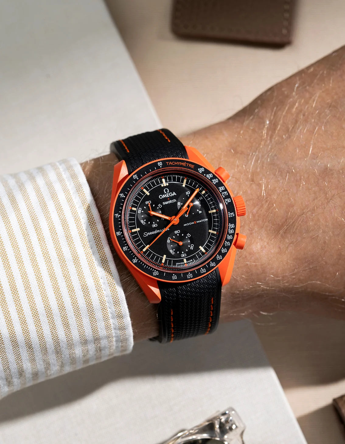 Wrist shot showing black rubber strap with orange stitching for Omega X Swatch MoonSwatch Mission On Earth Lava