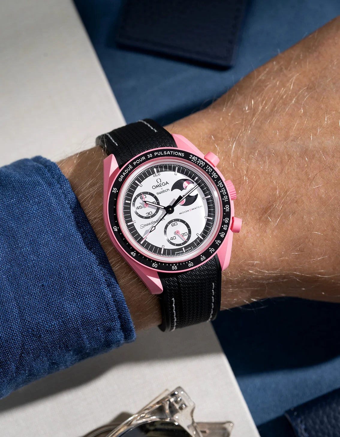 Wrist shot showing black rubber strap with white stitching for Omega X Swatch MoonSwatch Mission to the Pink Moonphase