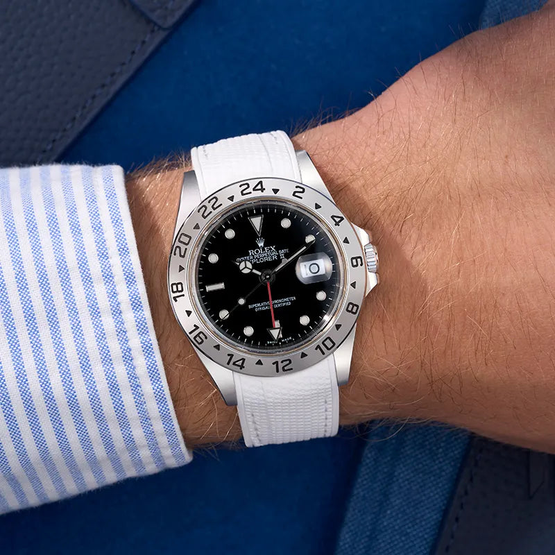 Rolex Explorer II 16570 with black dial and white Rolex Explorer rubber strap, styled on a wrist with a blue striped shirt background.