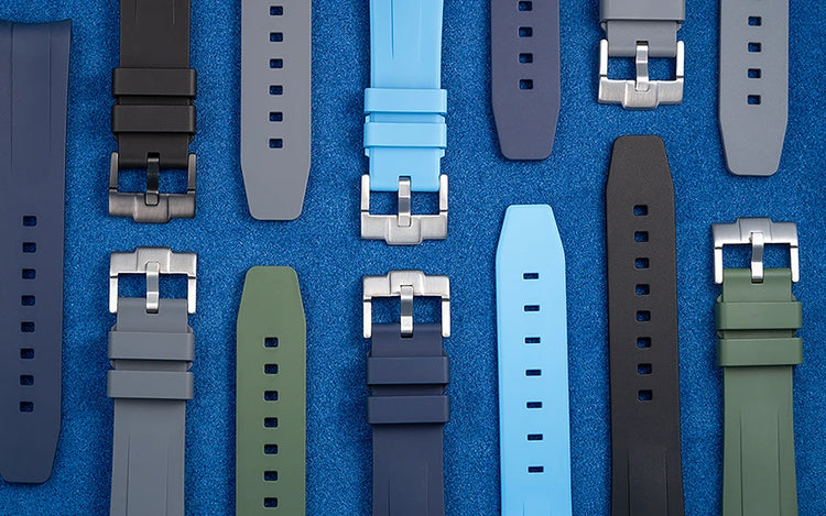 Collection of Wristbuddys FKM rubber straps in multiple colors including blue, black, grey, and green displayed on a blue background