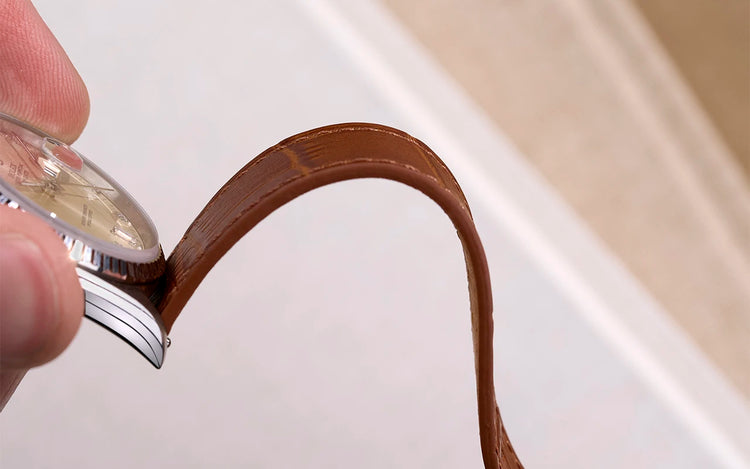 Hand inspecting a finished brown leather watch strap attached to a watch during the final quality control at Wristbuddys.