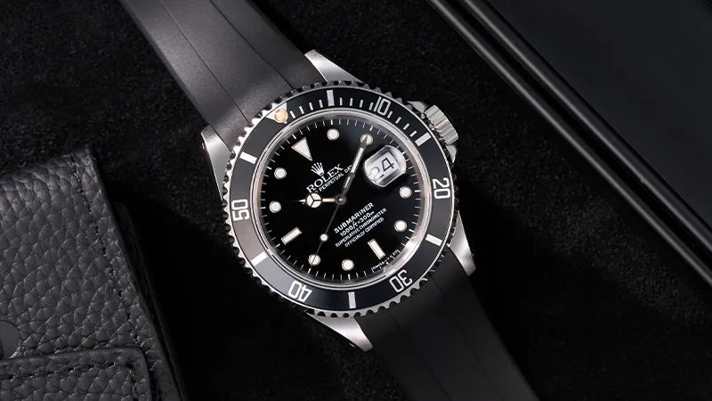 Rolex watch with a black rubber strap, displayed on a sleek black background, emphasizing its elegant and durable design.