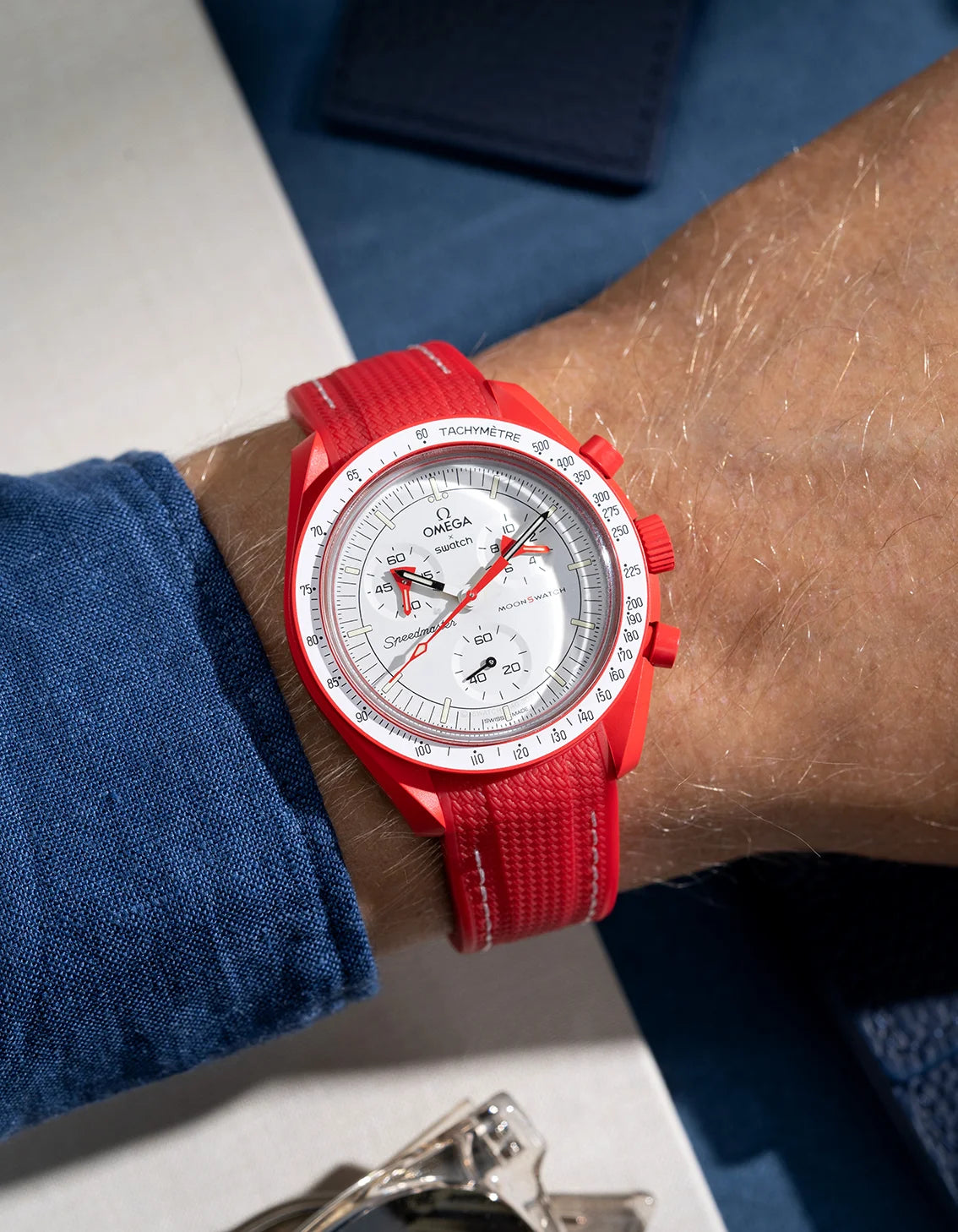 Red curved vertech rubber strap with white stitches photographed on a MoonSwatch Mission to Mars wrist shot