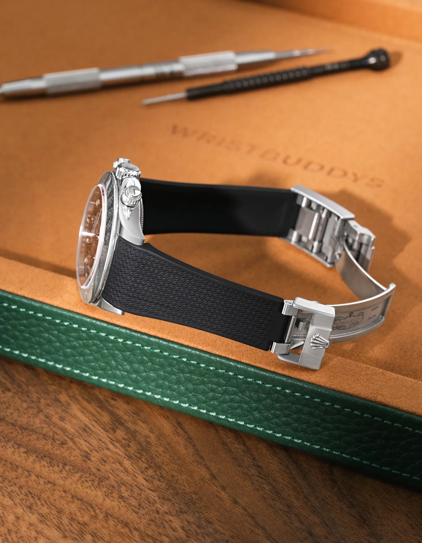 Black textured FKM rubber watch band for Rolex Daytona 116520, seamless case integration, mounted with original clasp on a leather valet tray.