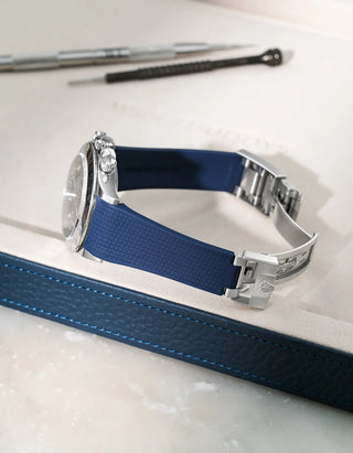 Navy Blue textured FKM rubber strap for Rolex Daytona 116520, integrated case fit for original clasp, resting on a blue leather valet tray.