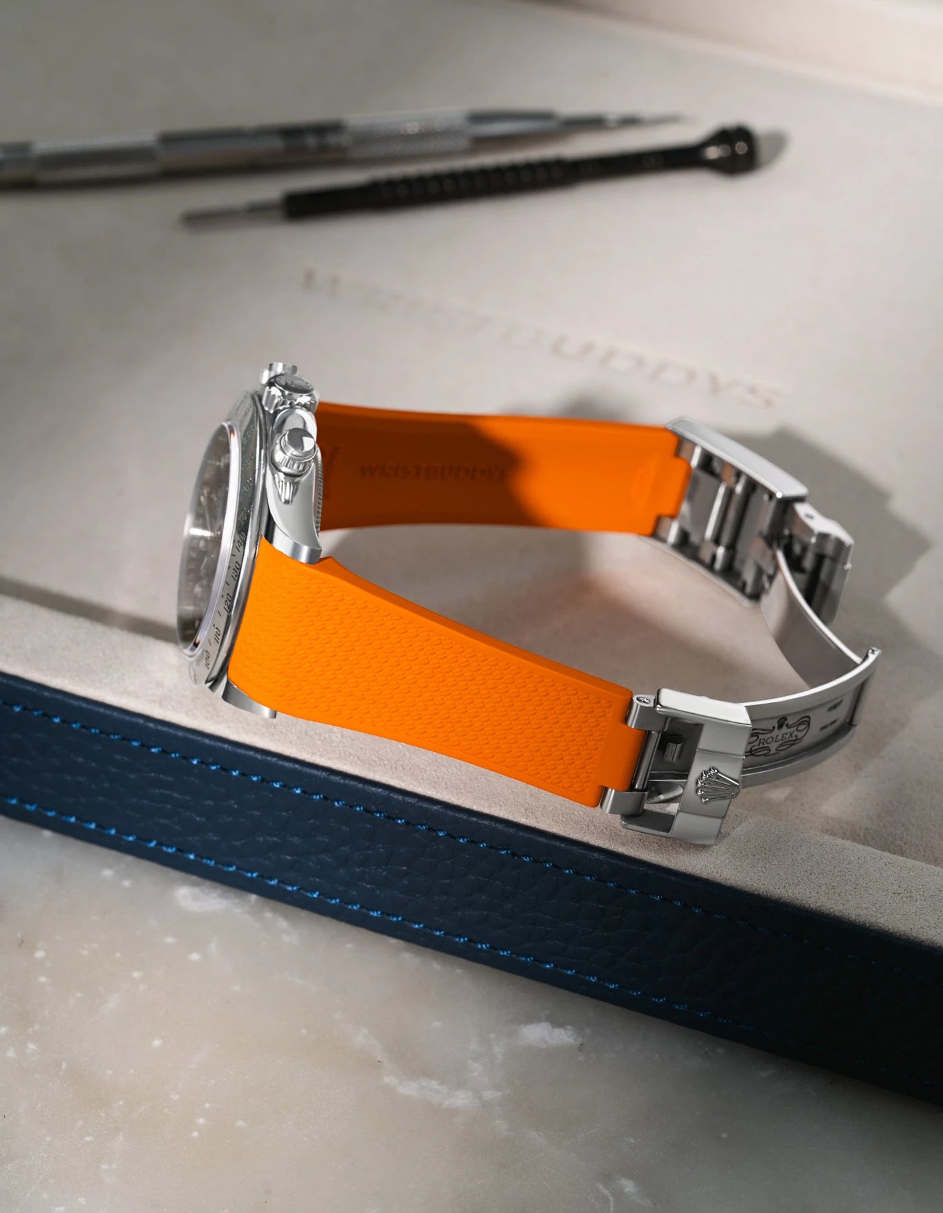 Orange Vertech FKM rubber strap for Rolex Daytona 116520, seamless integration with original oysterlock clasp, resting on a grey tray.