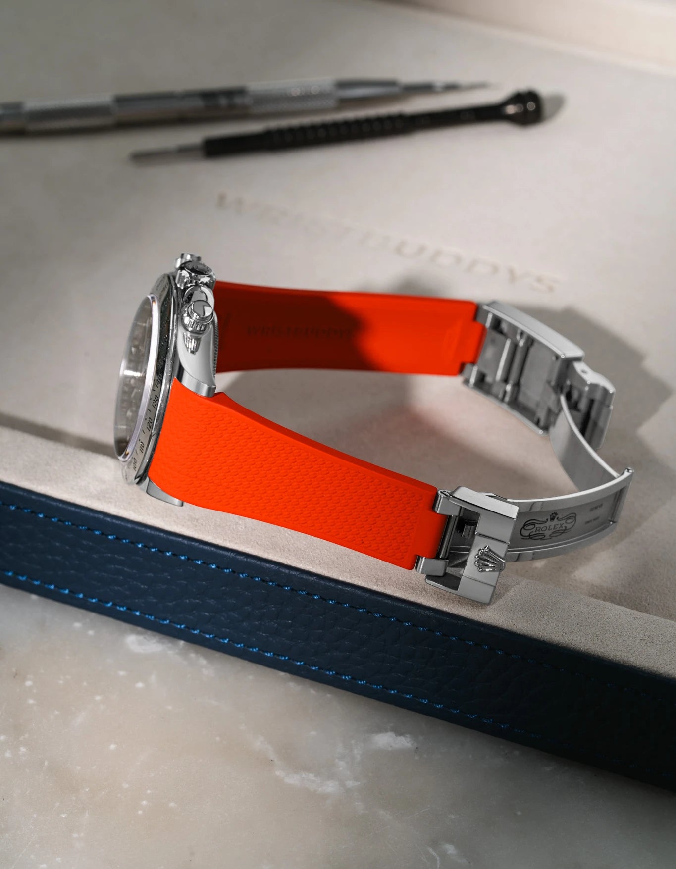 Red textured FKM rubber watch band for Rolex Daytona 116520, integrated design for original clasp, shown on a brown leather valet tray.