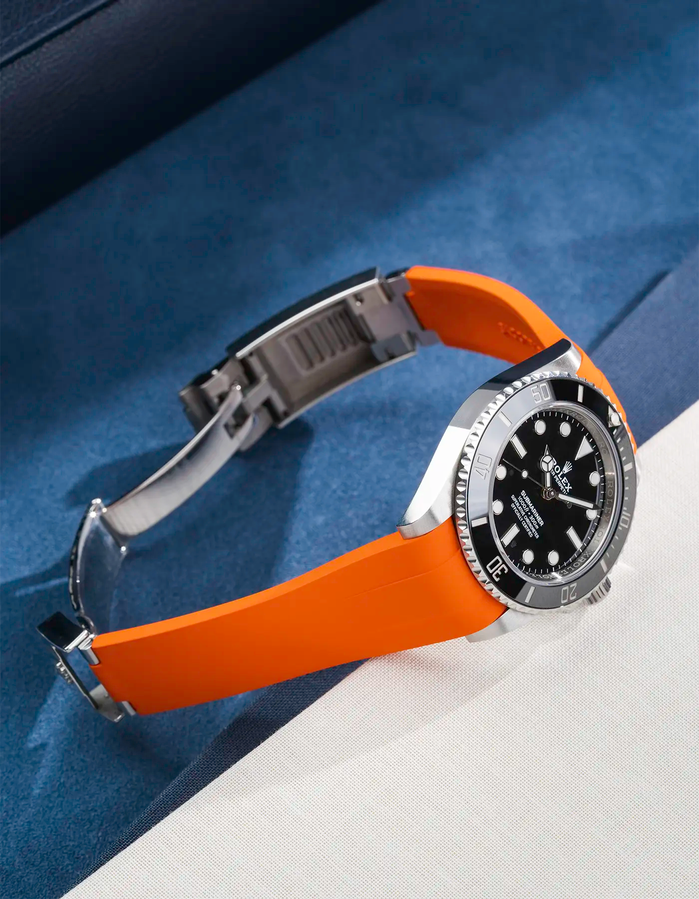 Lifestyle product photo of Rolex Submariner 41 with orange Classic Smooth FKM Rubber Strap mounted on the watch, integrated with original clasp – side angle view showing clasp open