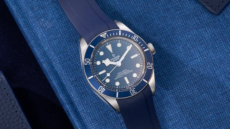 Tudor Black Bay watch with a blue rubber strap, part of the premium collection of straps for Tudor watches available at Wristbuddys, photographed on a matching blue fabric background.