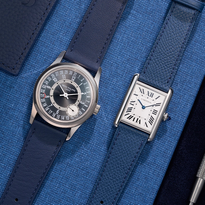 Patek Philippe and Cartier watches with blue universal leather straps displayed on a textured blue fabric background.