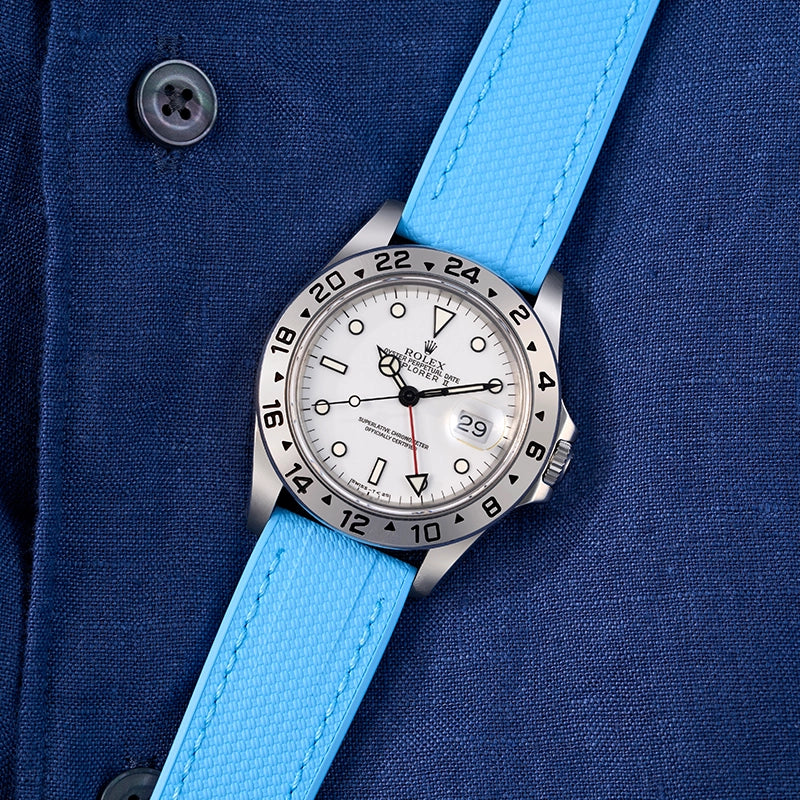 Rolex Explorer II with a white dial and a bright blue universal strap on a navy shirt background.