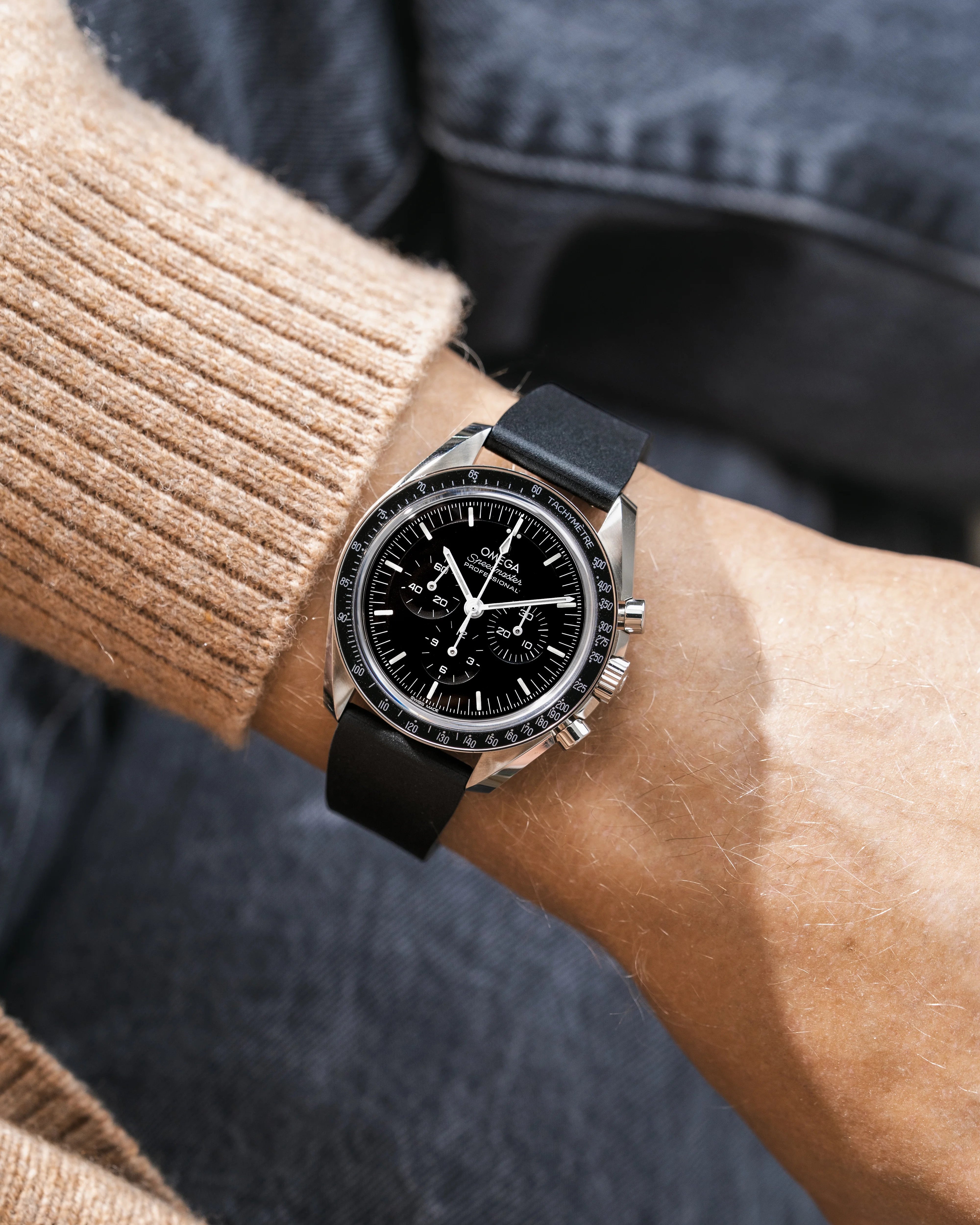 Close-up of a person's wrist wearing a black Omega Speedmaster with a FKM CTS Rubber watch strap from Wirstbuddys with a detailed face.
